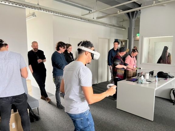 Ein Mann hat eine VR-Brille auf, hat VR-Controller in der Hand und scheint ein VR-Spiel zu spielen.